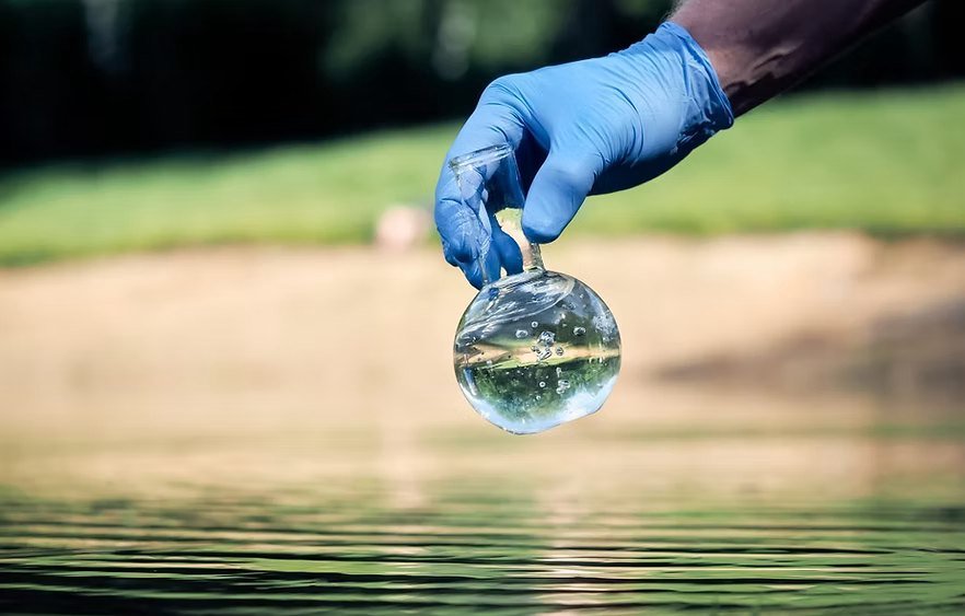 A gloved hand holding up a glass flask of lake water for testing